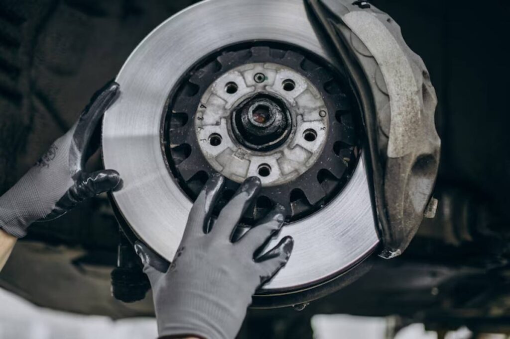 A mechanic wearing gloves is installing a shiny brake rotor on a car, focused on a close-up of the brake assembly.