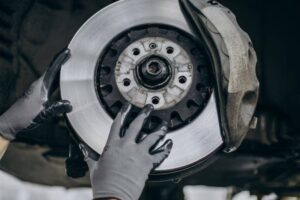 A mechanic wearing gloves is installing a shiny brake rotor on a car, focused on a close-up of the brake assembly.