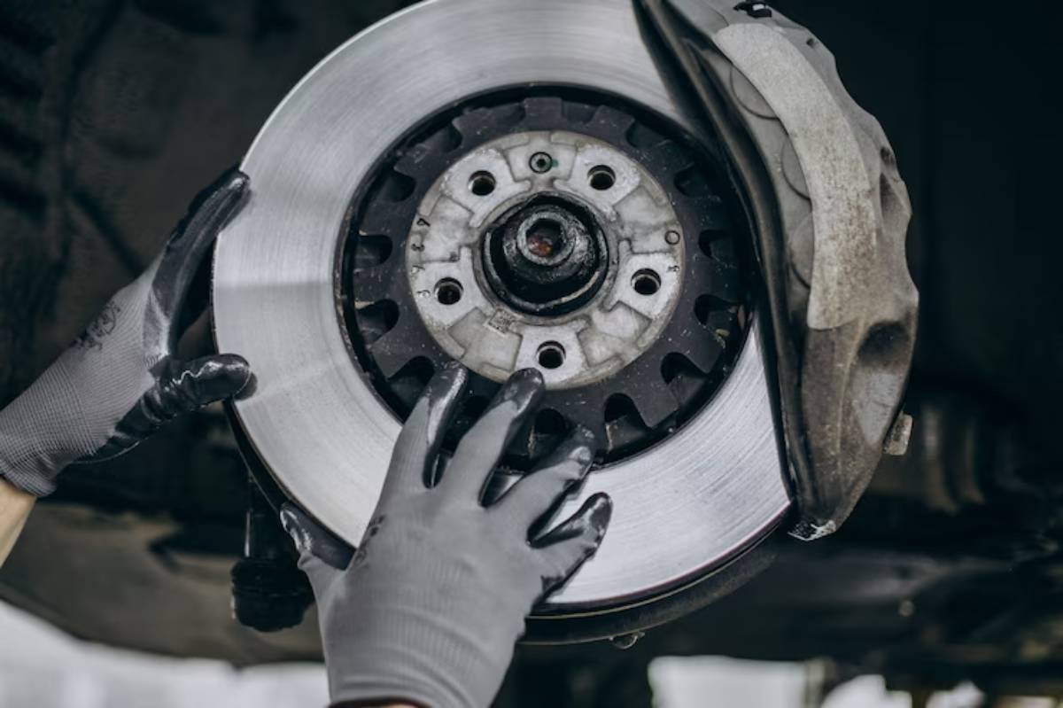 A mechanic wearing gloves is installing a shiny brake rotor on a car, focused on a close-up of the brake assembly.