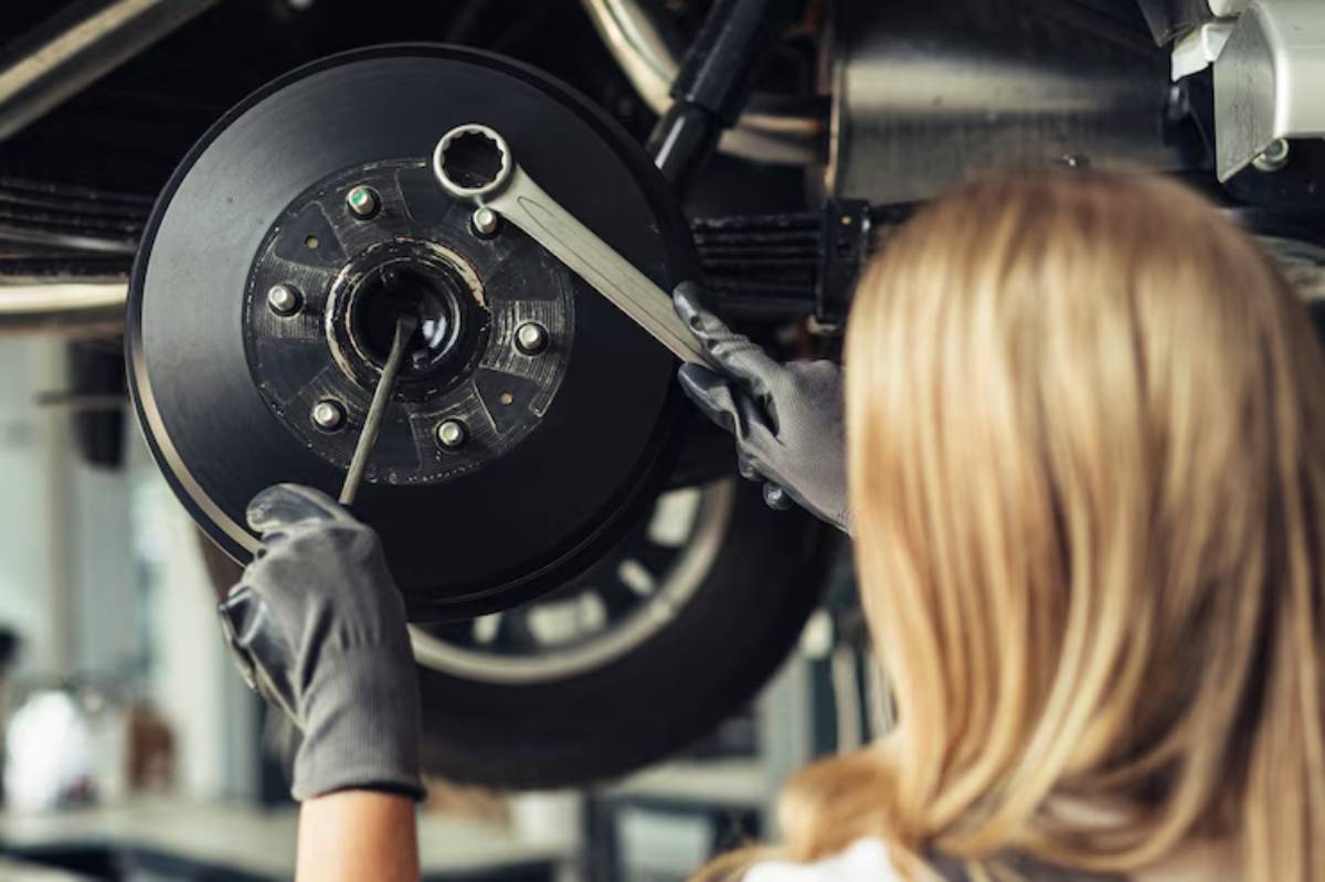 A mechanic wearing gloves works on a car's brake assembly, using a wrench and tool, focused on the intricate components.