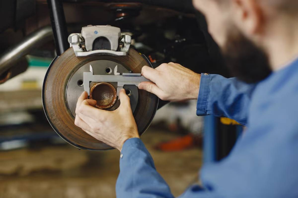 A mechanic measures a brake rotor using calipers, focusing intently on precise measurements in a garage setting.