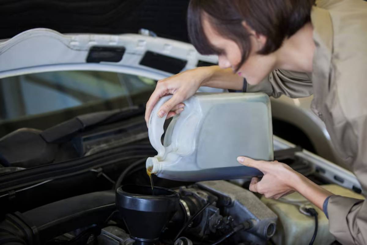 A woman pours motor oil from a jug into a funnel placed over an engine in a car’s hood, focused on the task.