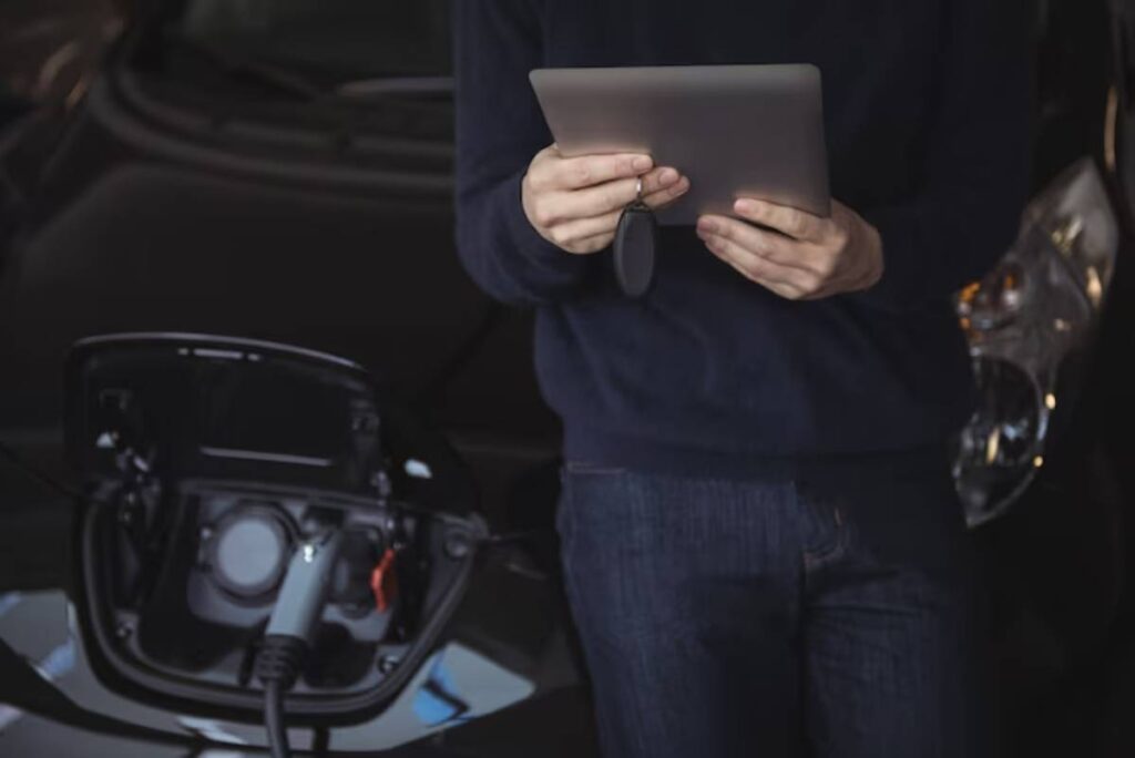 A person holding a tablet near an electric vehicle charging port, focusing on the charging process.