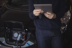 A person holding a tablet near an electric vehicle charging port, focusing on the charging process.
