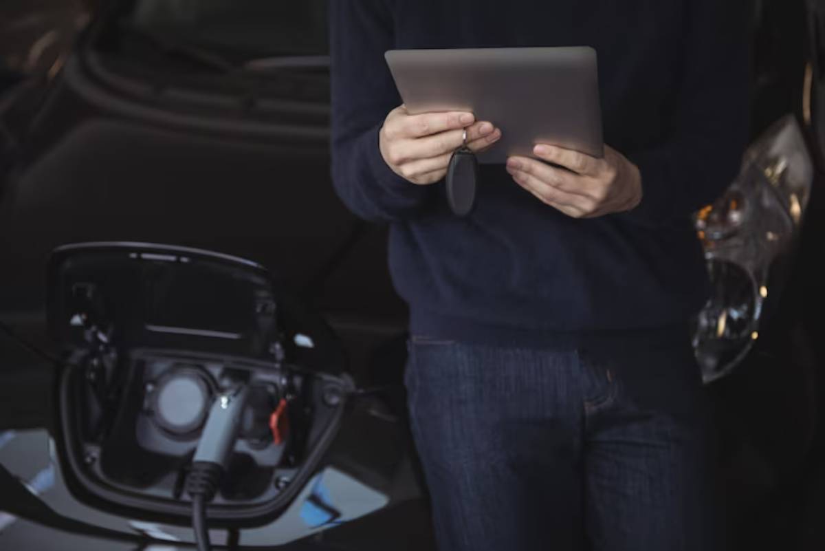 A person holding a tablet near an electric vehicle charging port, focusing on the charging process.