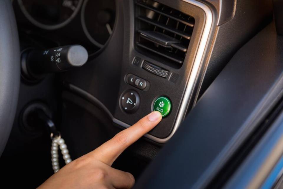 A hand pressing the green 'ECO' button in a car's console, promoting fuel efficiency and environmentally friendly driving.