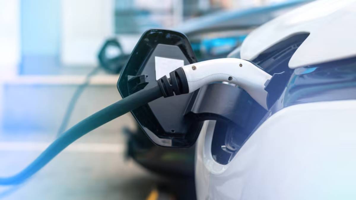 Close-up of an electric vehicle charging cable connected to a white car at a charging station.