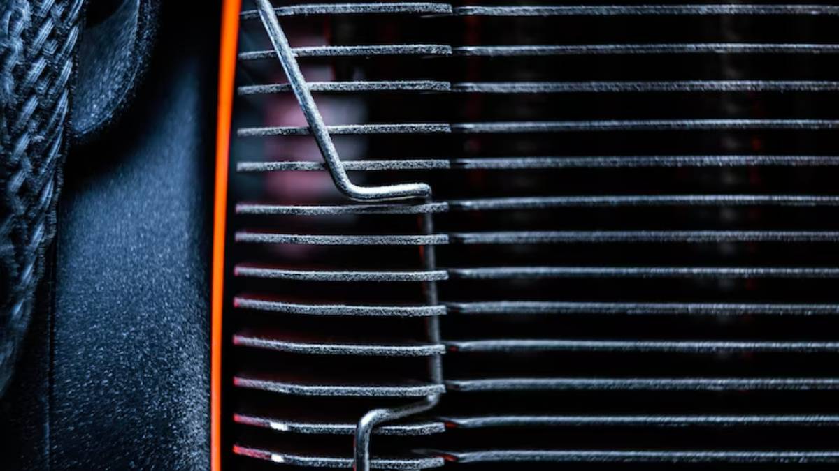 Close-up of a metal heat sink with closely spaced fins, featuring a thin wire support, set against a dark background.