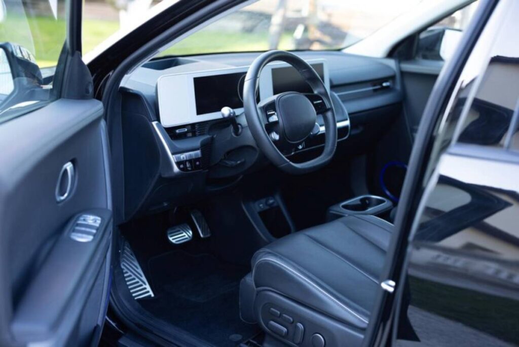 Interior view of a modern car showcasing a sleek dashboard, large display screens, and black leather seating.