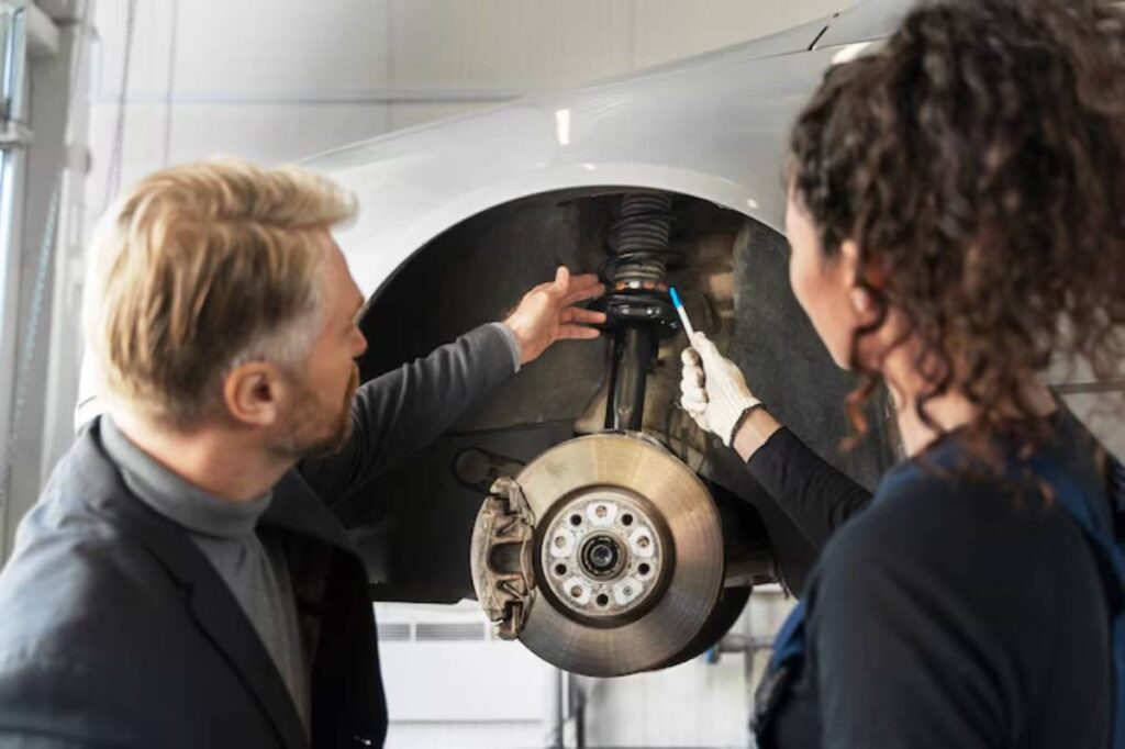 A mechanic inspects a car's suspension and brake components, discussing repairs in a well-lit garage.