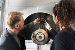 A mechanic inspects a car's suspension and brake components, discussing repairs in a well-lit garage.