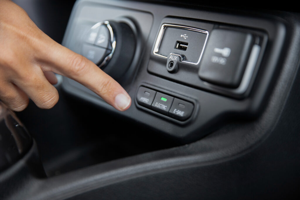 A hand presses the 'Electric' button on a vehicle's control panel, surrounded by various input and drive mode options.