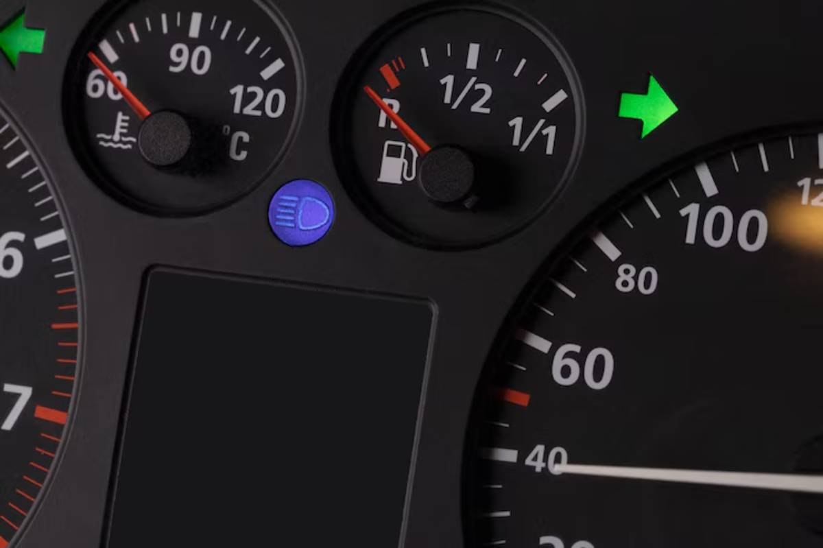 Close-up of a car dashboard showing fuel gauge, temperature gauge, and indicator lights for headlights and turn signals.