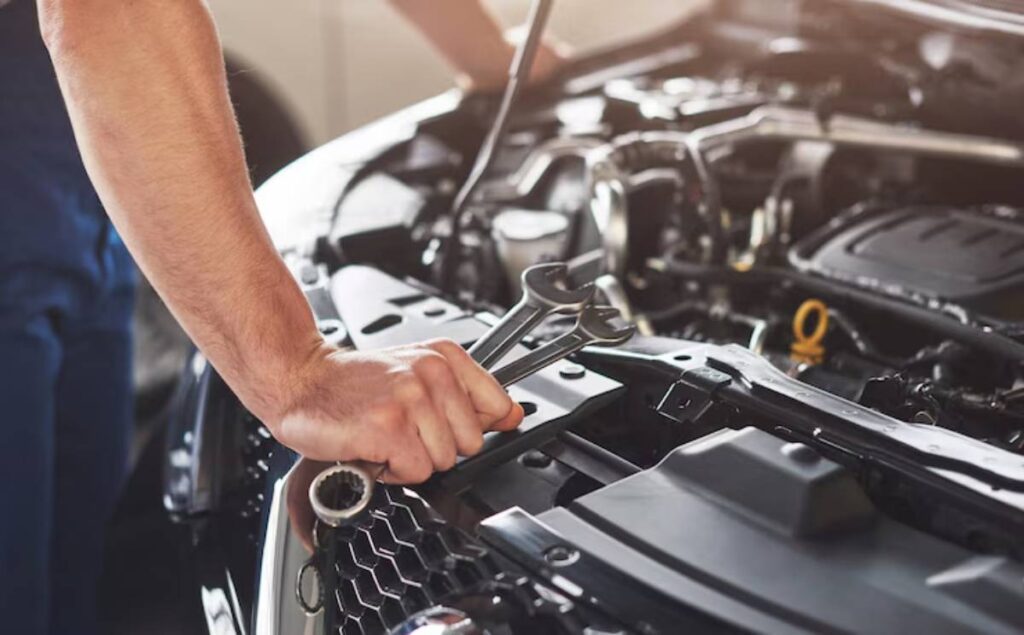 A mechanic's hand holds a wrench over a car engine, working on repairs in a bright garage.