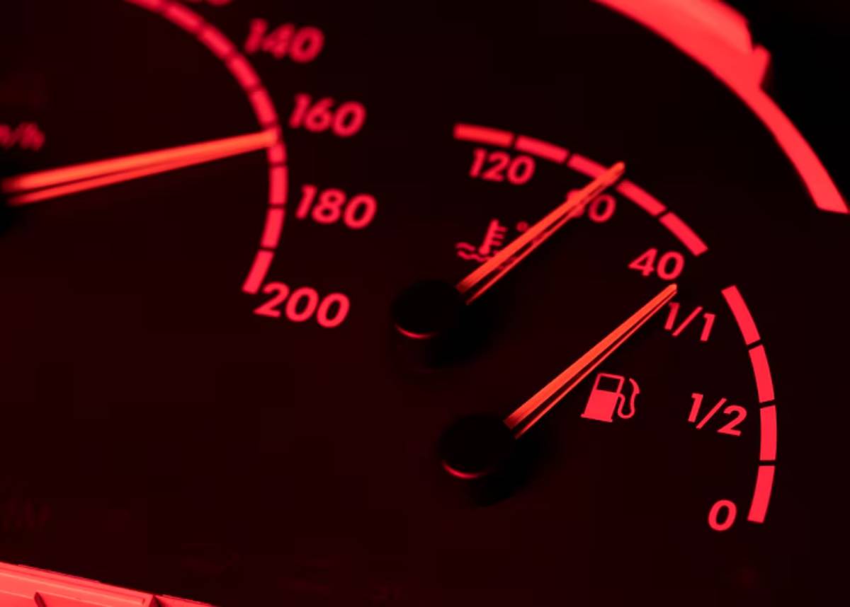 Close-up of a car dashboard showing speedometer and fuel gauge in red lighting, with speed nearing 160 km/h and fuel below half.