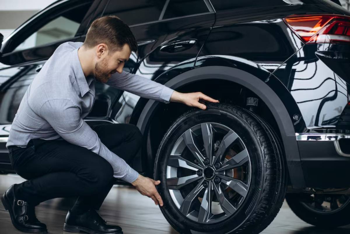 A man inspects the tire of a sleek black car while squatting in a well-lit showroom.