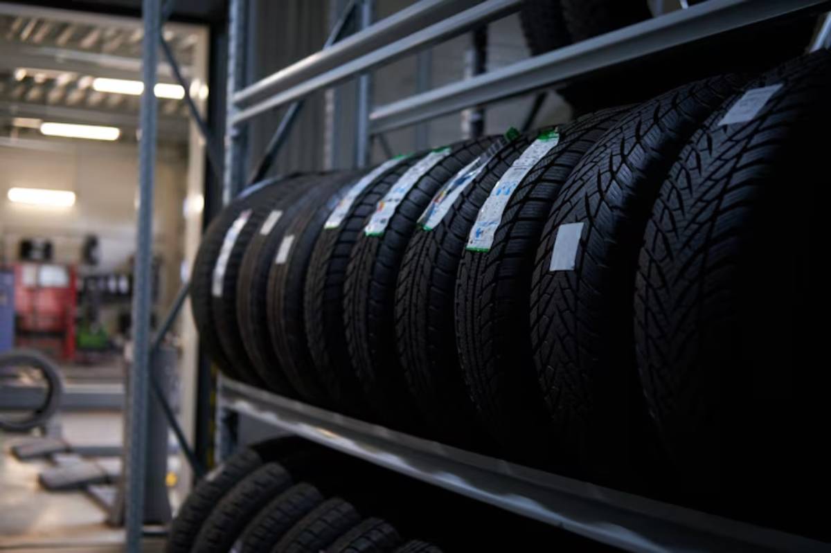 Rows of new tires displayed on metal racks in a well-lit tire shop, each labeled with price tags and specifications.