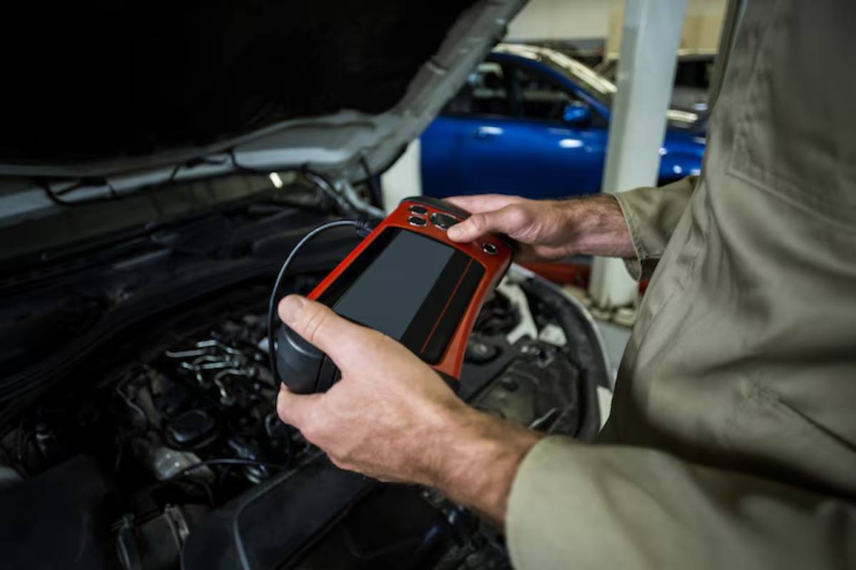 A man inspects a car engine using a handheld device for diagnostics.
