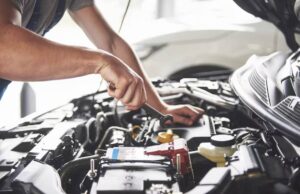 A mechanic repairs a car engine, using a wrench to tighten components under the hood in a well-lit garage.