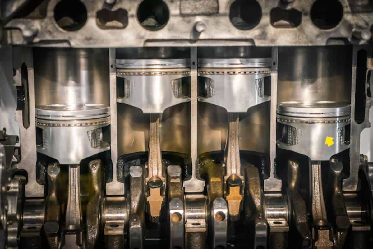 Close-up of an engine's internal components, featuring three pistons, connecting rods, and a crankshaft in metallic hues.