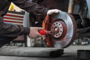 A mechanic inspects and works on a car's brake system using a ratchet tool, wearing gloves in a workshop setting.