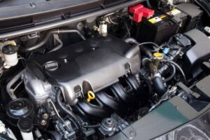 Close-up of a car engine bay showing the engine block, battery, and various components like hoses and fluid reservoirs.
