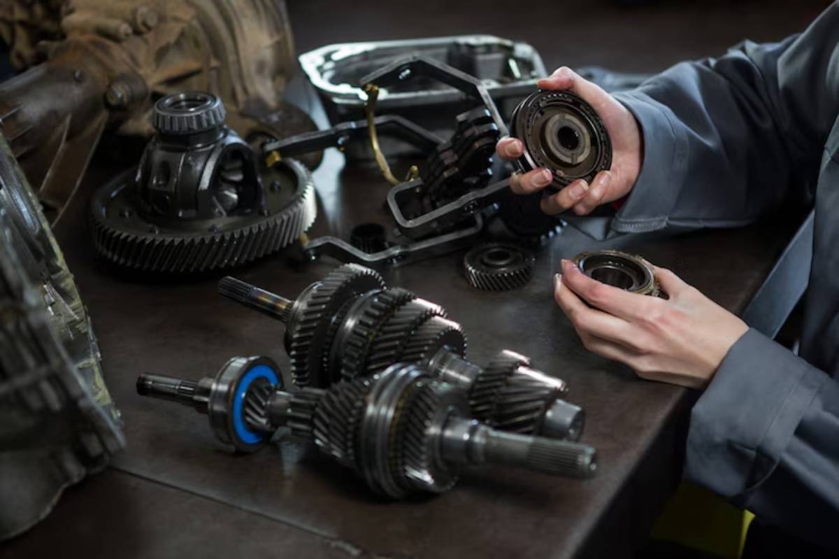 A mechanic examines gears and transmission parts on a workbench, highlighting hands engaged in automotive repair.