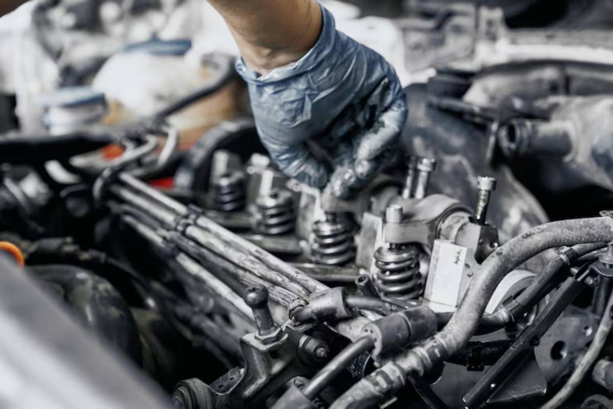 A mechanic in blue gloves works on a car engine, adjusting valve springs amidst various engine components.