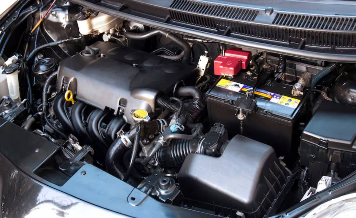 Close-up of a car engine compartment, featuring a battery, fluid reservoirs, and multiple connected hoses and components.