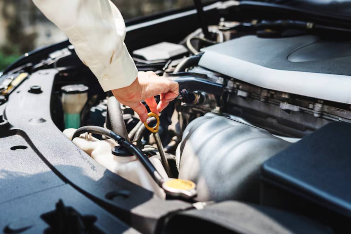 A person in a light shirt checks the oil level in a car engine, holding an oil dipstick above the engine compartment.