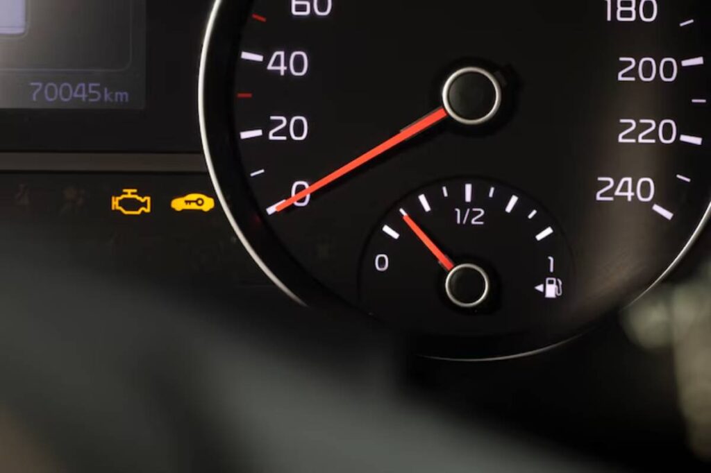 Close-up of a car dashboard showing the speedometer at 0, fuel gauge at half, and warning lights for engine and key security.