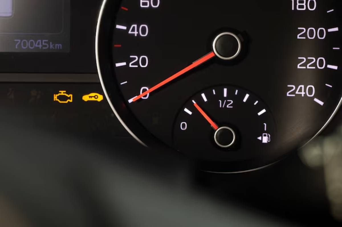 Close-up of a car dashboard showing the speedometer at 0, fuel gauge at half, and warning lights for engine and key security.
